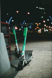 Žmogus važiuoja elektriniu paspirtuku vakare miesto gatvėje su apšvietimu