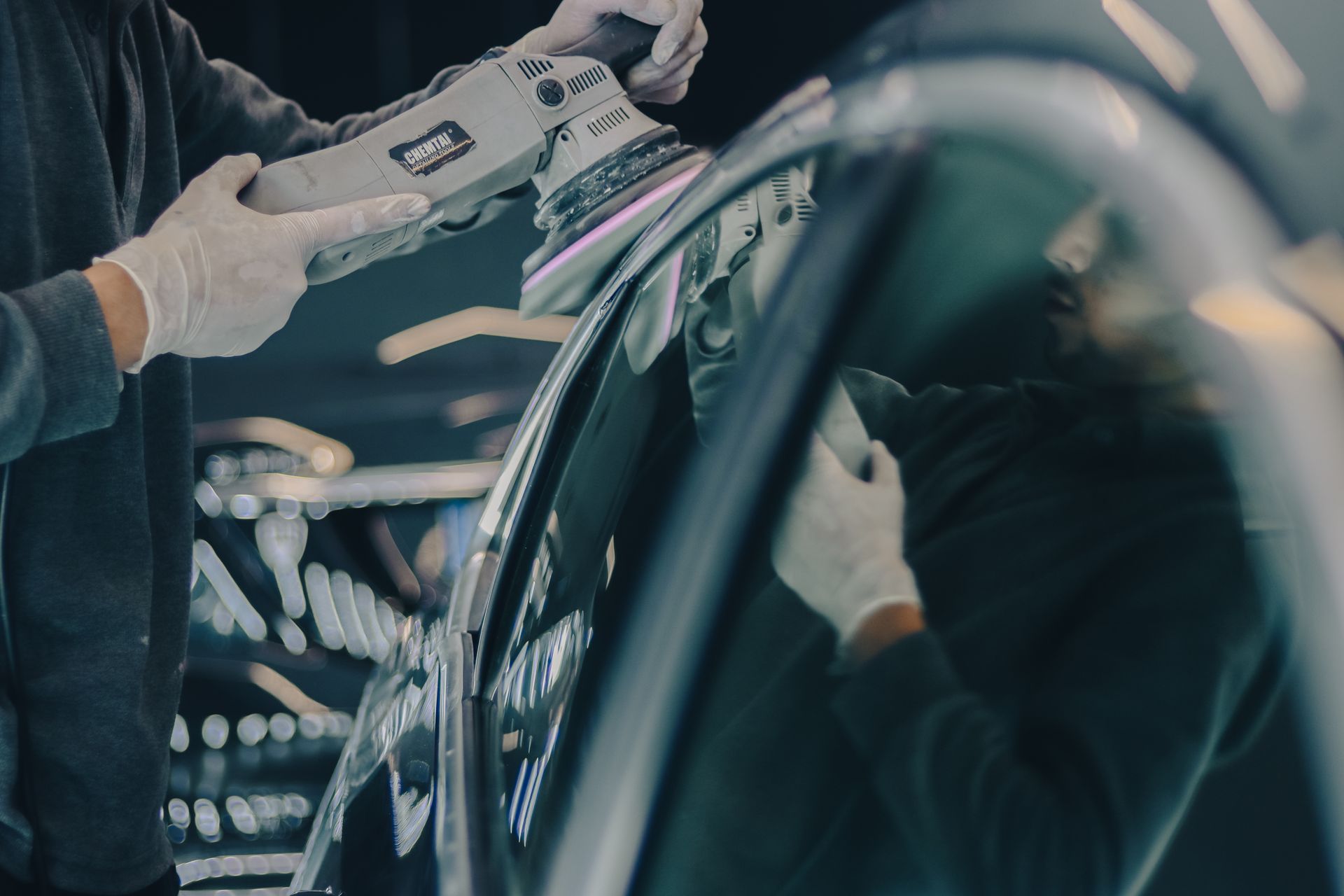 Vyras poliravimo mašinėle atnaujina tamsaus automobilio kėbulo laką garaže